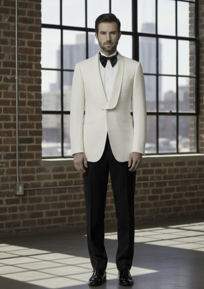 Man wearing a white tuxedo with a black bow tie in front of large windows with a cityscape view.
