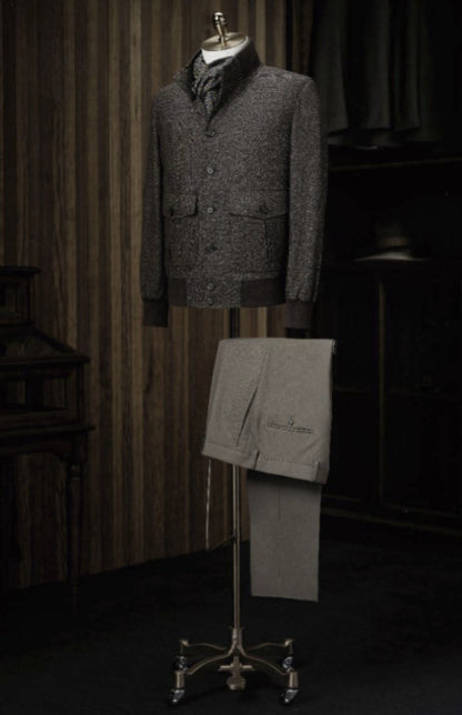 Mannequin wearing a grey textured jacket with a matching scarf, standing next to a folded gray garment on a stand against a dark background.