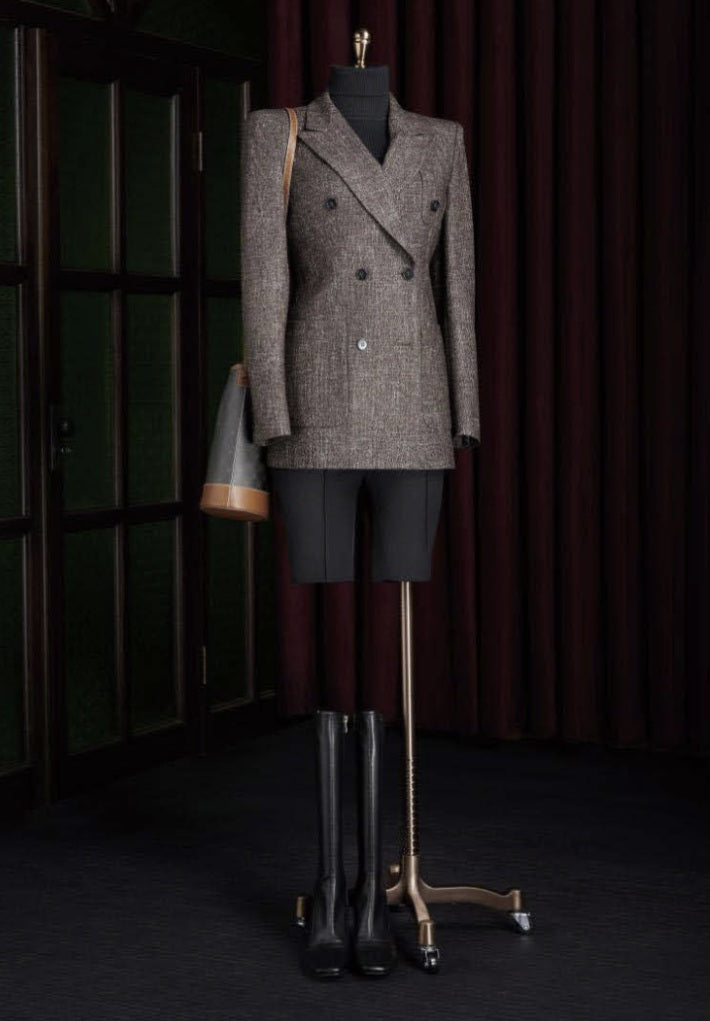 Mannequin wearing a tweed jacket and black skirt with a handbag against a dark background
