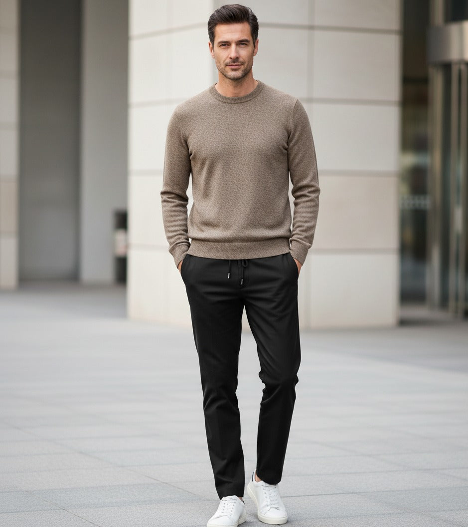 Man wearing a brown sweater and black pants standing in an urban setting.