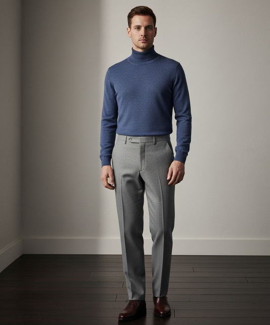 Man wearing a blue turtleneck sweater and gray pants against a plain background