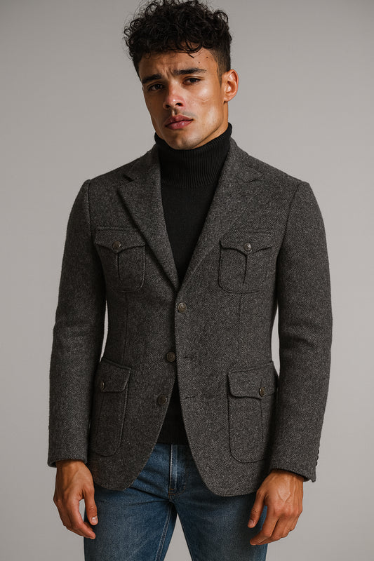 Man wearing a gray blazer over a black turtleneck and blue jeans on a gray background