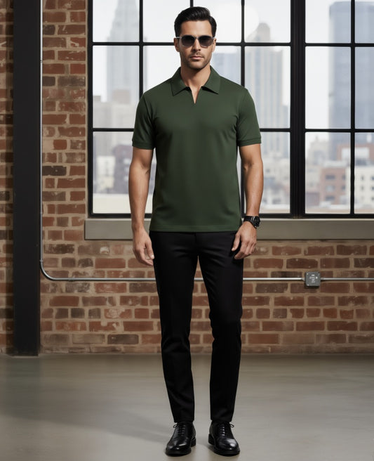 Man wearing a green polo shirt and black pants standing in front of a large window with a cityscape view.