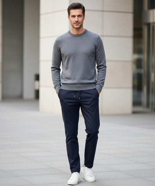 Man wearing a gray sweater and navy pants standing in front of a building.