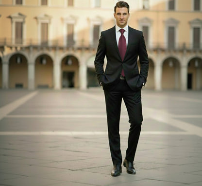 Man in a black suit with a red tie standing in an open square with arches in the background.