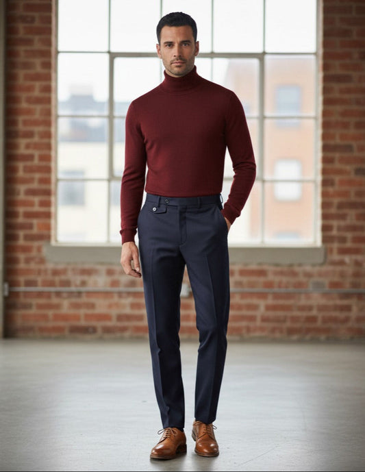 Man wearing a red turtleneck sweater and dark pants standing in front of a brick wall with large windows.
