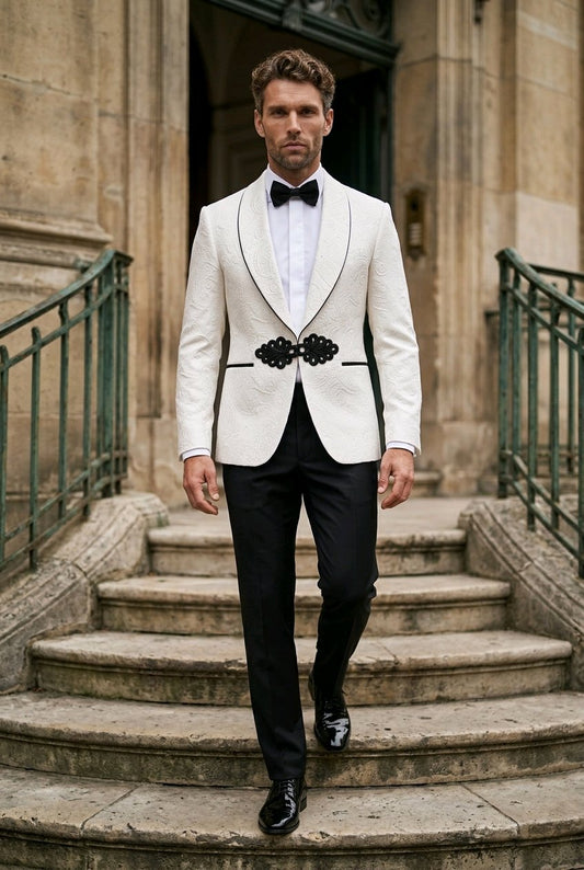 A man wearing a white tuxedo jacket with black satin lapels and a decorative black bow tie, walking down stone stairs in front of a historic building.