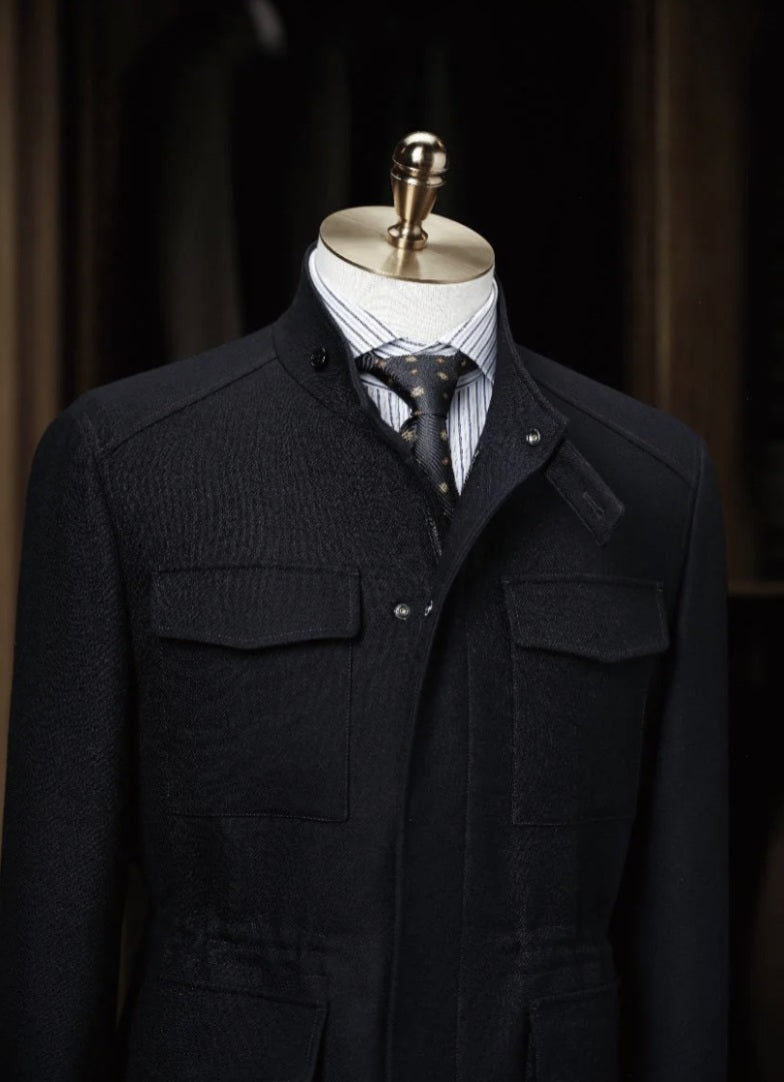 Black coat on a mannequin with a striped shirt and tie against a dark background