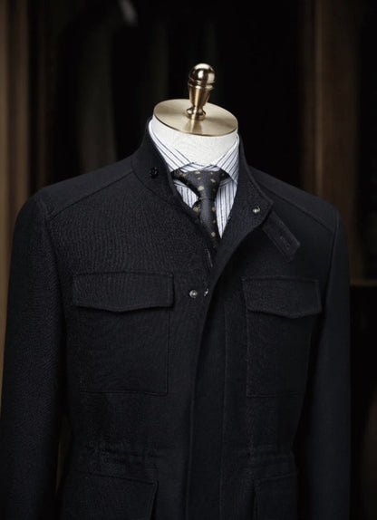 Black coat on a mannequin with a striped shirt and tie against a dark background