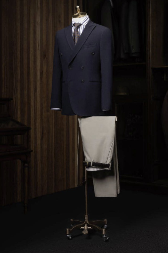 Navy suit jacket and beige pants on a stand against a wooden wall.