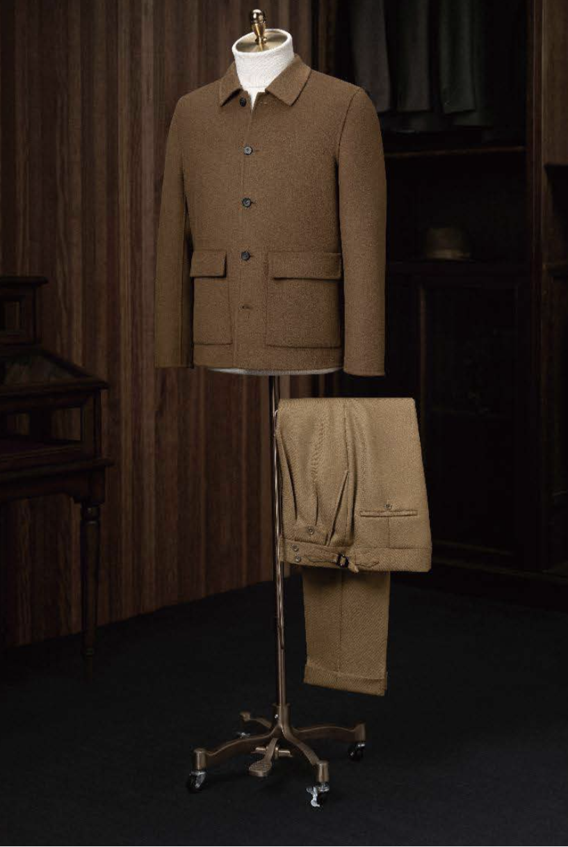 A tan casual jacket and tan twill trousers displayed on a mannequin, with the jacket featuring a high shirt collar, front pockets, and dark brown buttons. The trousers have a waistband and side adjusters.