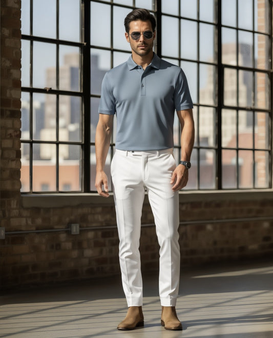 Man wearing a Teal polo shirt and white pants standing in a room with large windows.