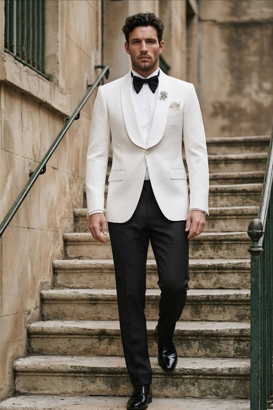 A man walks down outdoor stone stairs wearing a white tuxedo jacket with black trousers, a white shirt, a black bow tie, and a black dress shoe.