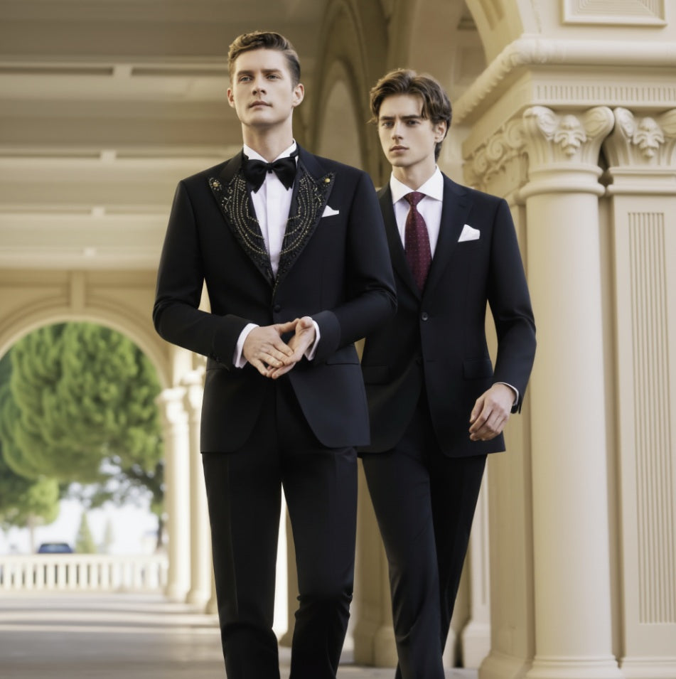 Two men wearing black tuxedos with gold brocade peaked lapels, single-breasted design, and black buttons, standing in a columned hallway.