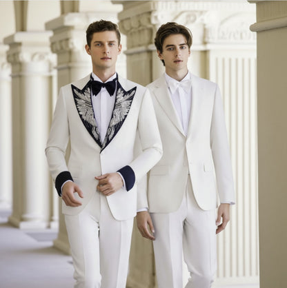 Two men wearing white tuxedos with black satin lapels and bow ties, standing in a columned hallway.