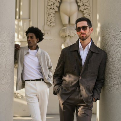 Two people standing against a decorative wall, one wearing sunglasses and a dark coat.