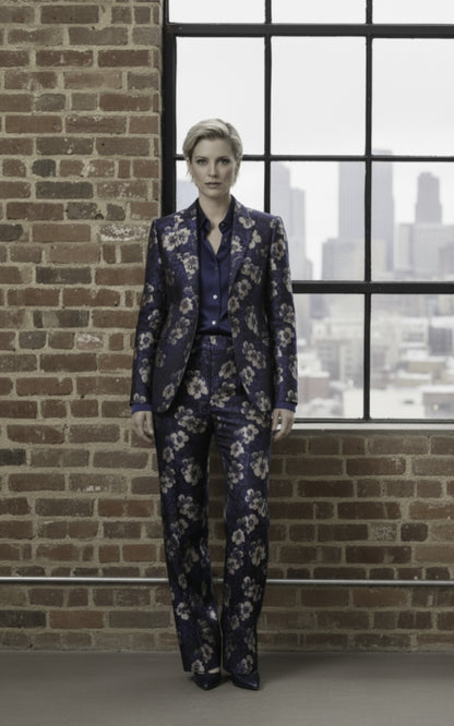 Person wearing a floral suit standing against a brick wall with a window view.