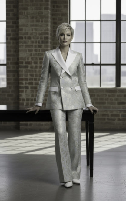 Woman in a gray suit standing in a room with large windows and brick walls.