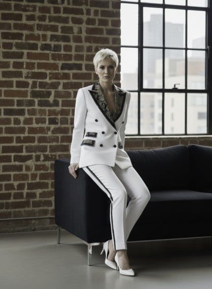 Woman in a white suit sitting on a black couch against a brick wall with large windows.