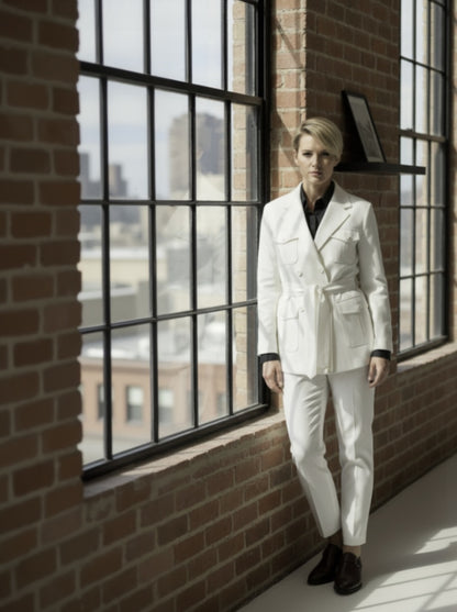 Woman in a white suit standing by a large window with a brick wall background