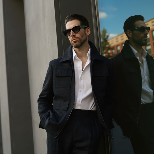 A man wearing a black linen herringbone zip-up jacket with matching trousers, standing outdoors.