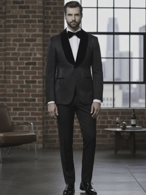 Man in a black tuxedo standing in a room with brick walls and large windows.