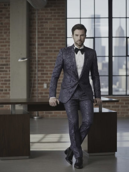 Man wearing a dark patterned suit with a white shirt and black bow tie in an urban setting.